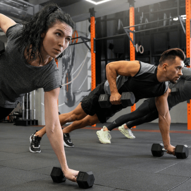 Two people performing dumbbell plank rows in a gym