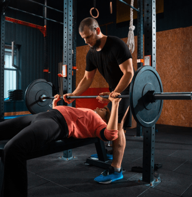 Trainer spotting a woman during a barbell bench press